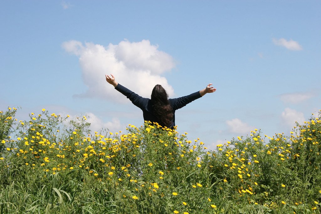 Persona respirando aire libre con los brazos abiertos en un campo de flores